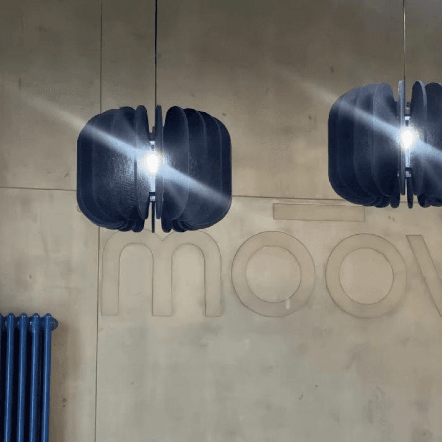 Логотип Moov на бетонной стене под двумя чёрными светильниками
